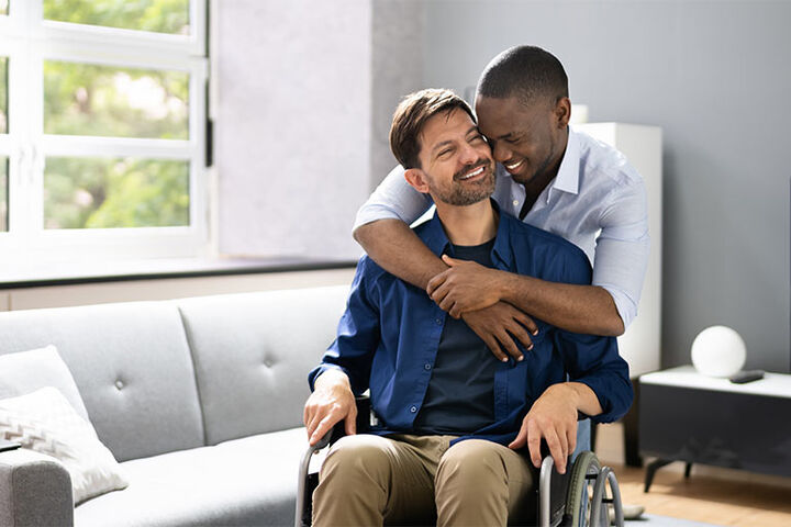 A man in a wheelchair is embraced by another man.